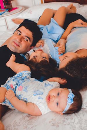 Family lying together on white bedding during lifestyle photo session with baby.
