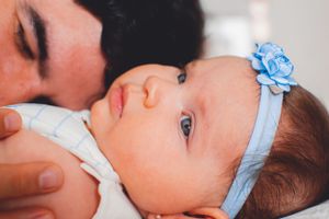 Baby wearing blue floral headband gazes up while being held in tender close-up portrait.