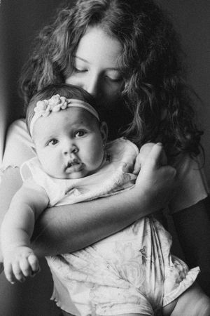 Black and white portrait of baby with headband being held tenderly.