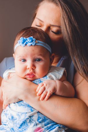 Baby in blue floral outfit and headband being cuddled in close-up portrait.