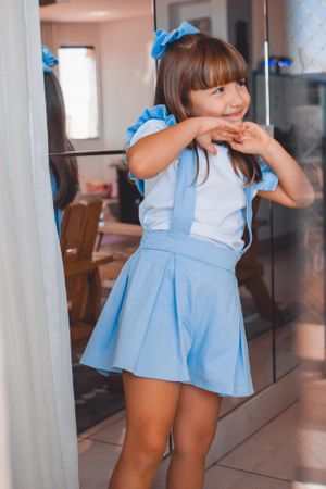 Child wearing a blue dress dancing and smiling in front of a mirror.