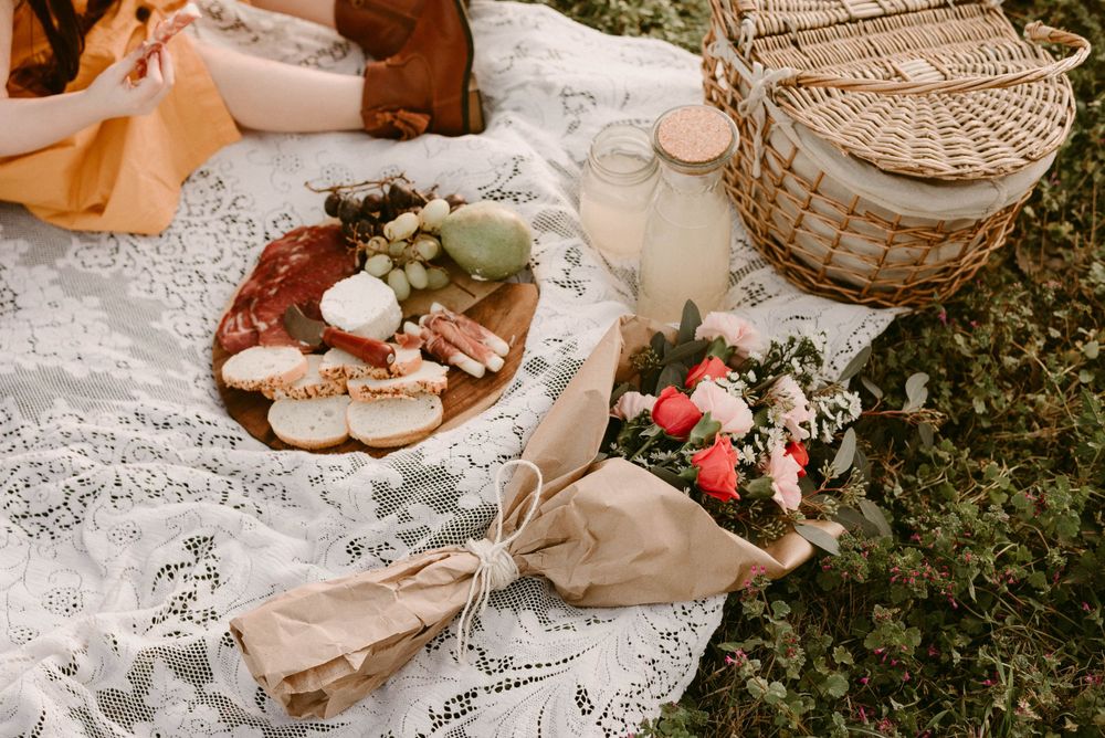Rustic picnic setup with lace blanket, wicker basket, and snacks laid out on grass.
