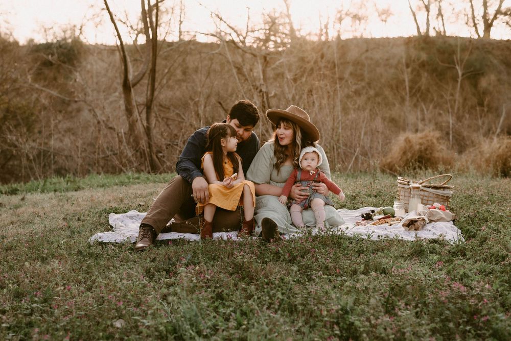 A family enjoying a sunset picnic together on a white blanket outdoors.