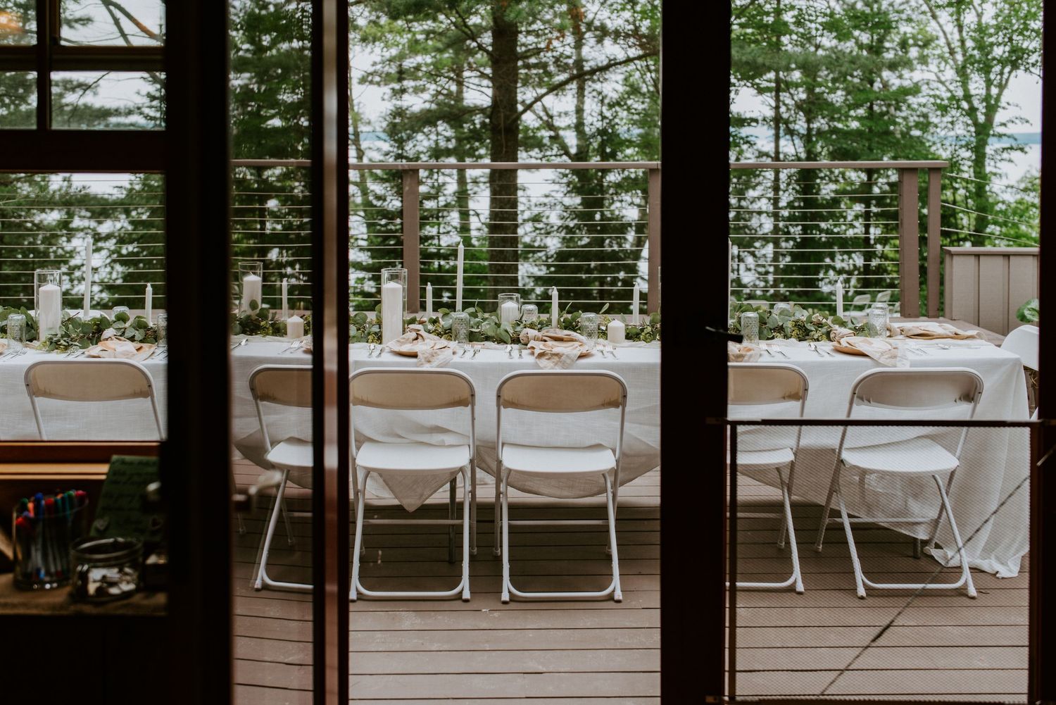 A wedding head table is decorated with eucalyptus, silver forks, and wooden plates with tall white candles and mason jar