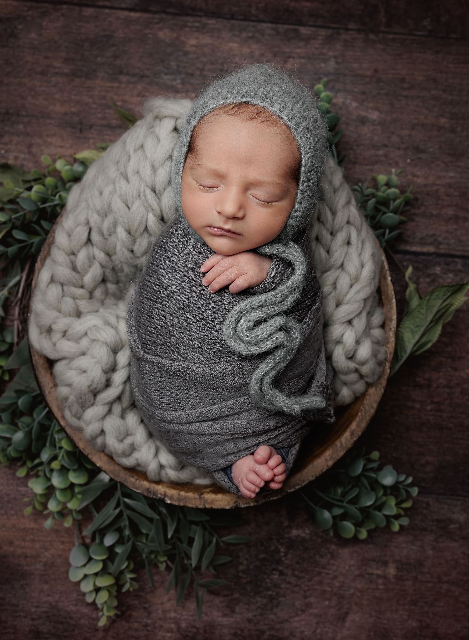 newborn boy posed in a bowl with greenery and sage knitted bonnet by Austin Newborn photography