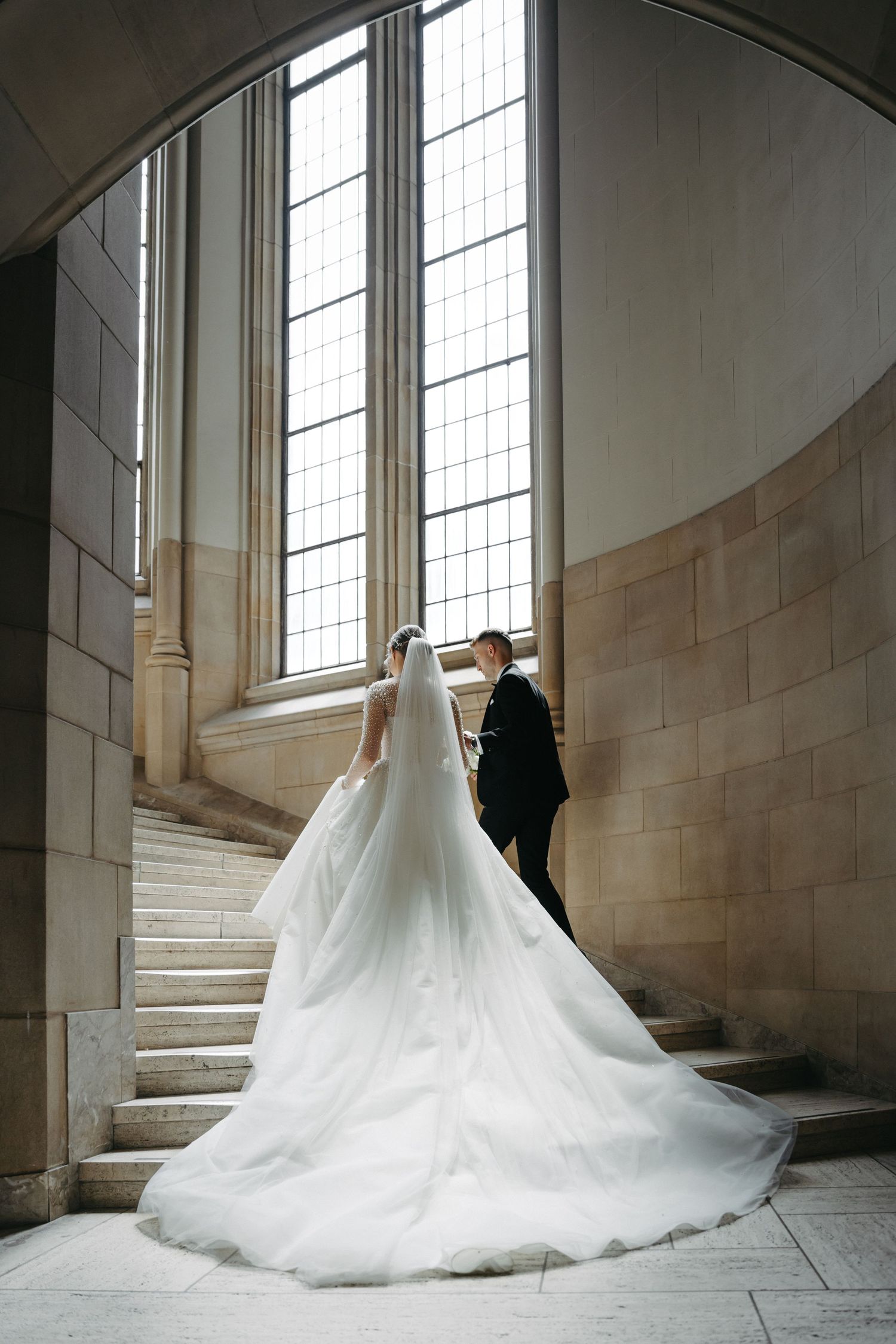 Wedding dress with dramatic long train flowing down stone steps near tall windows.