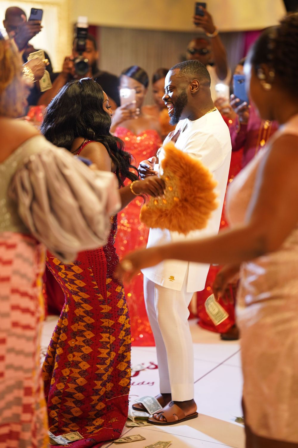 Celebration scene with people in traditional African attire dancing at indoor event.