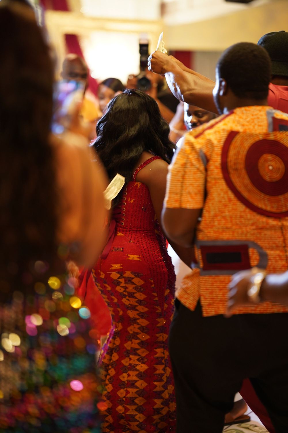 People in colorful traditional African clothing dancing at indoor celebration.