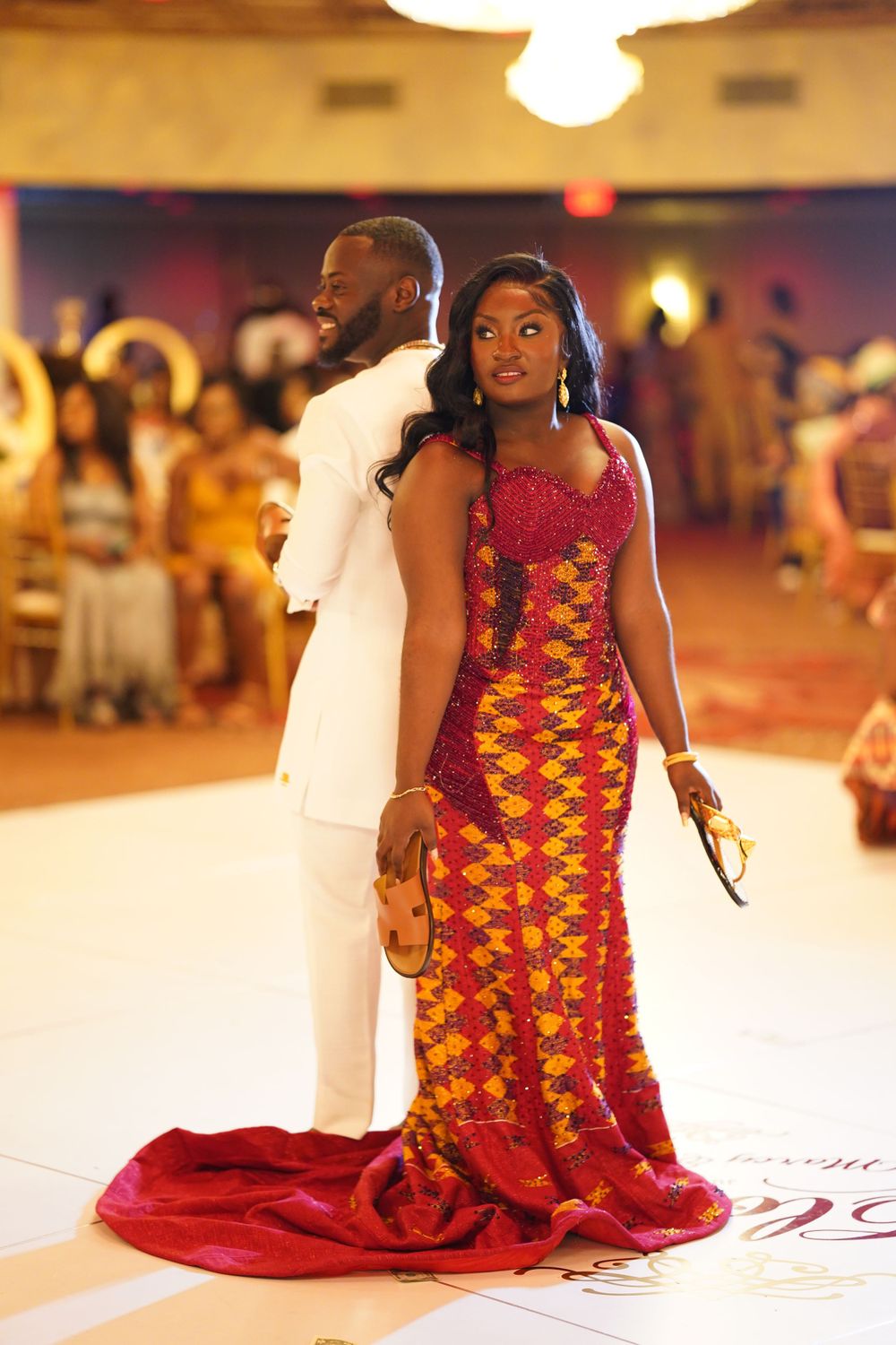 Formal couple strikes elegant pose in white suit and traditional African print gown with red train.