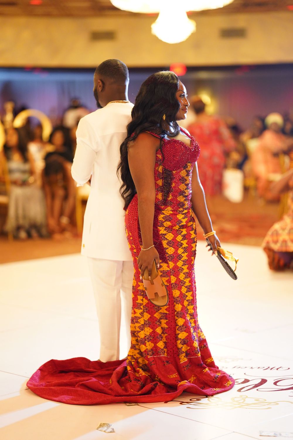Elegant couple poses in white suit and African print gown with flowing red train.