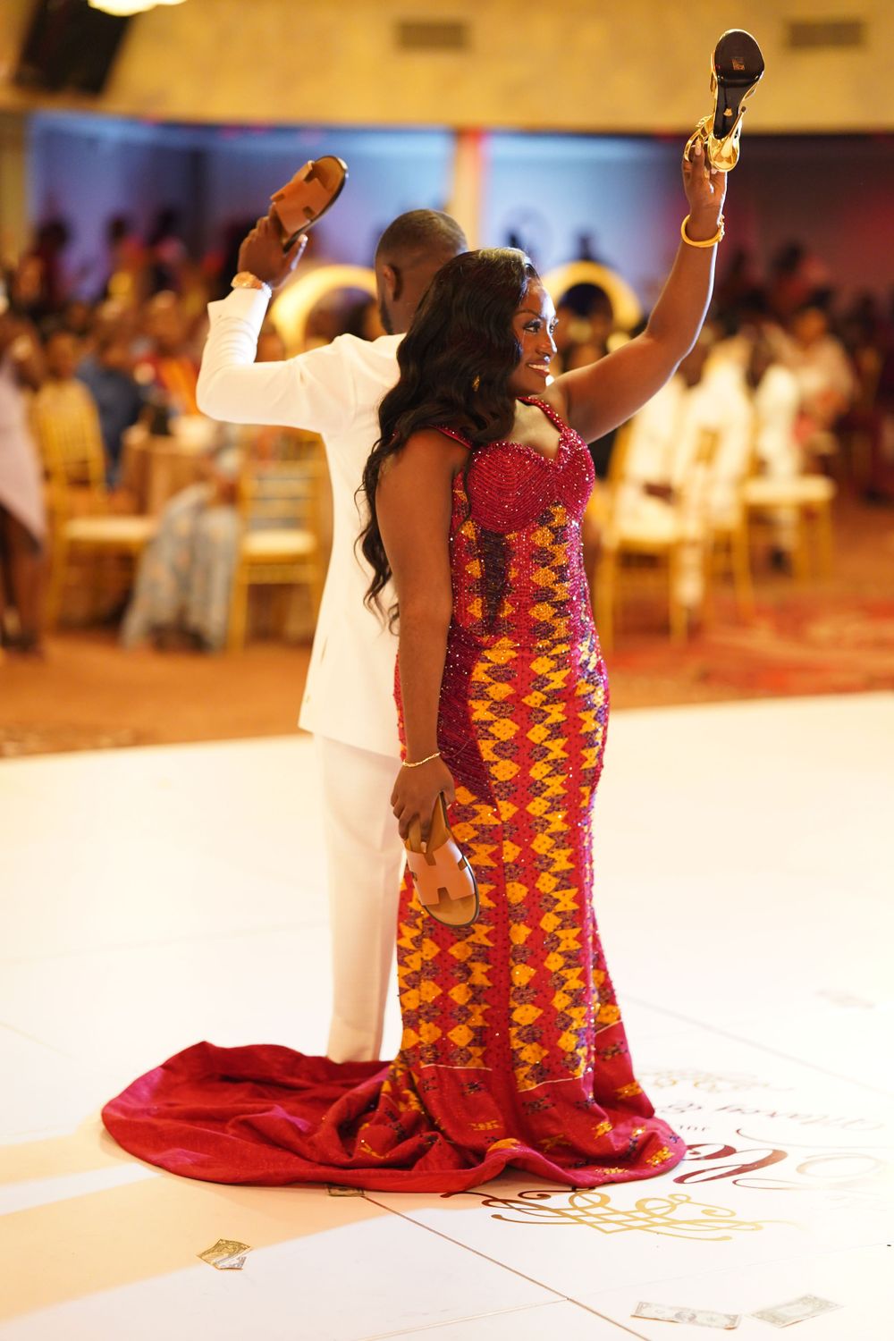 Celebratory moment with raised arms during formal event in white and patterned attire.