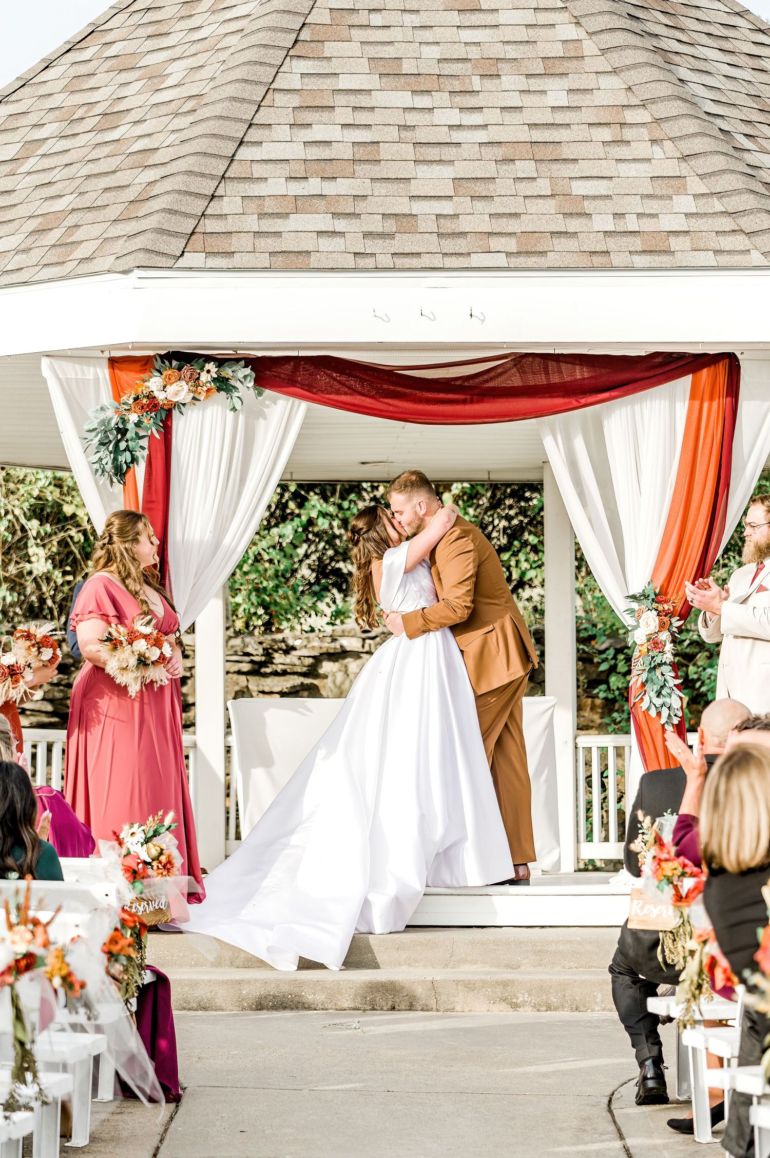 A wedding ceremony takes place under a decorated white gazebo with coral draping and floral arrangements by Stephanie Coulter Photography