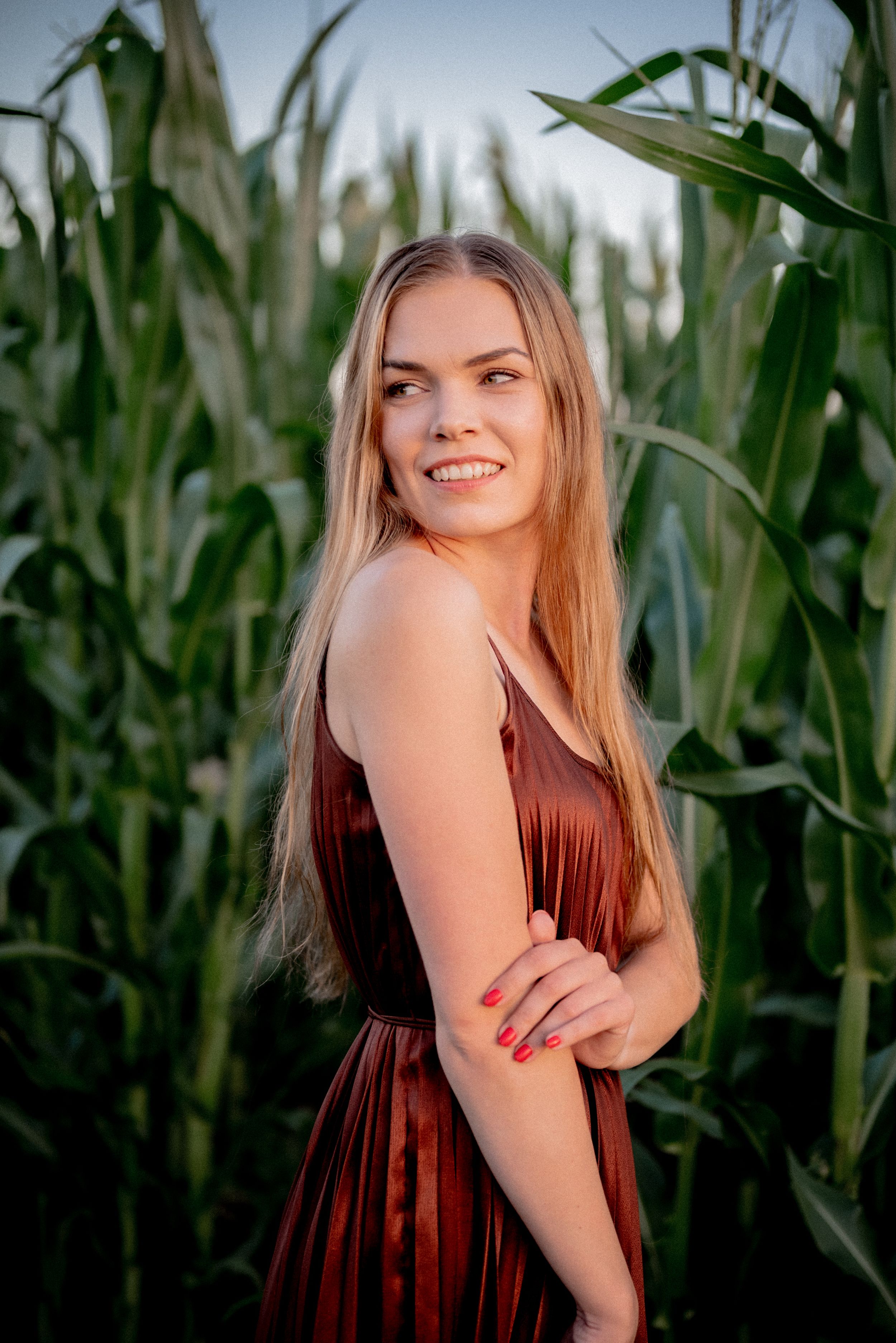 Summer portrait in brown dress against cornfield at golden hour.