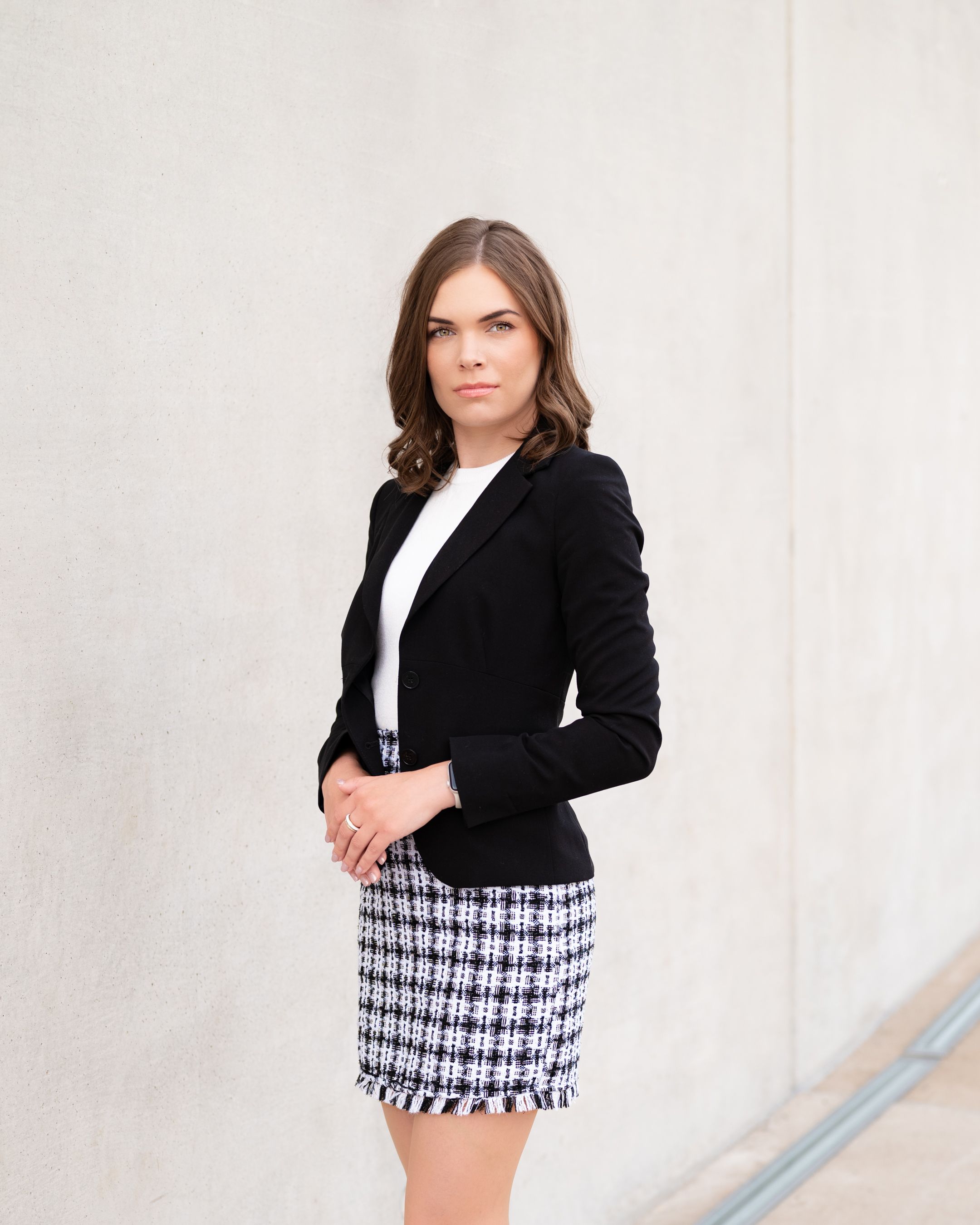 Classic professional attire with black blazer and patterned skirt in studio setting.