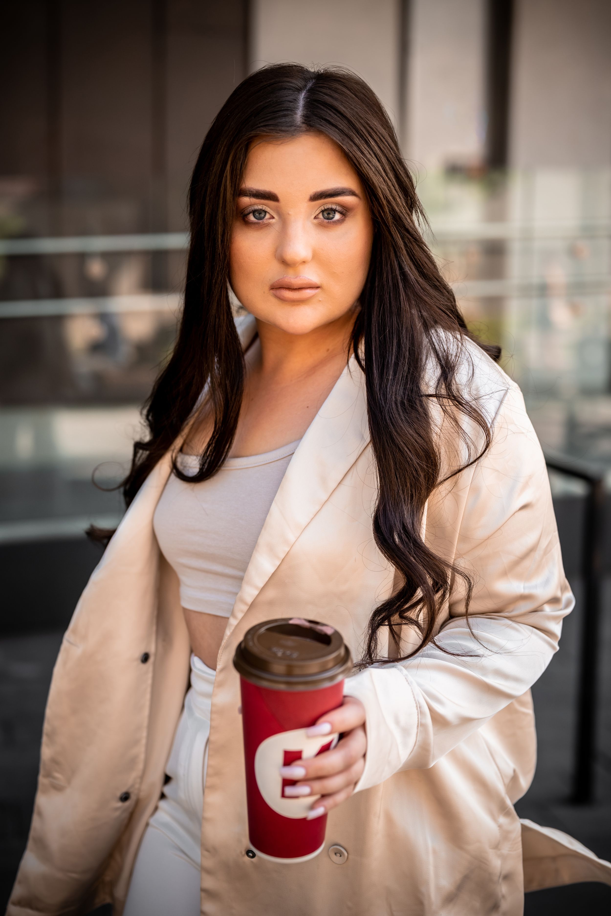 Urban fashion shot with beige blazer and red coffee cup.