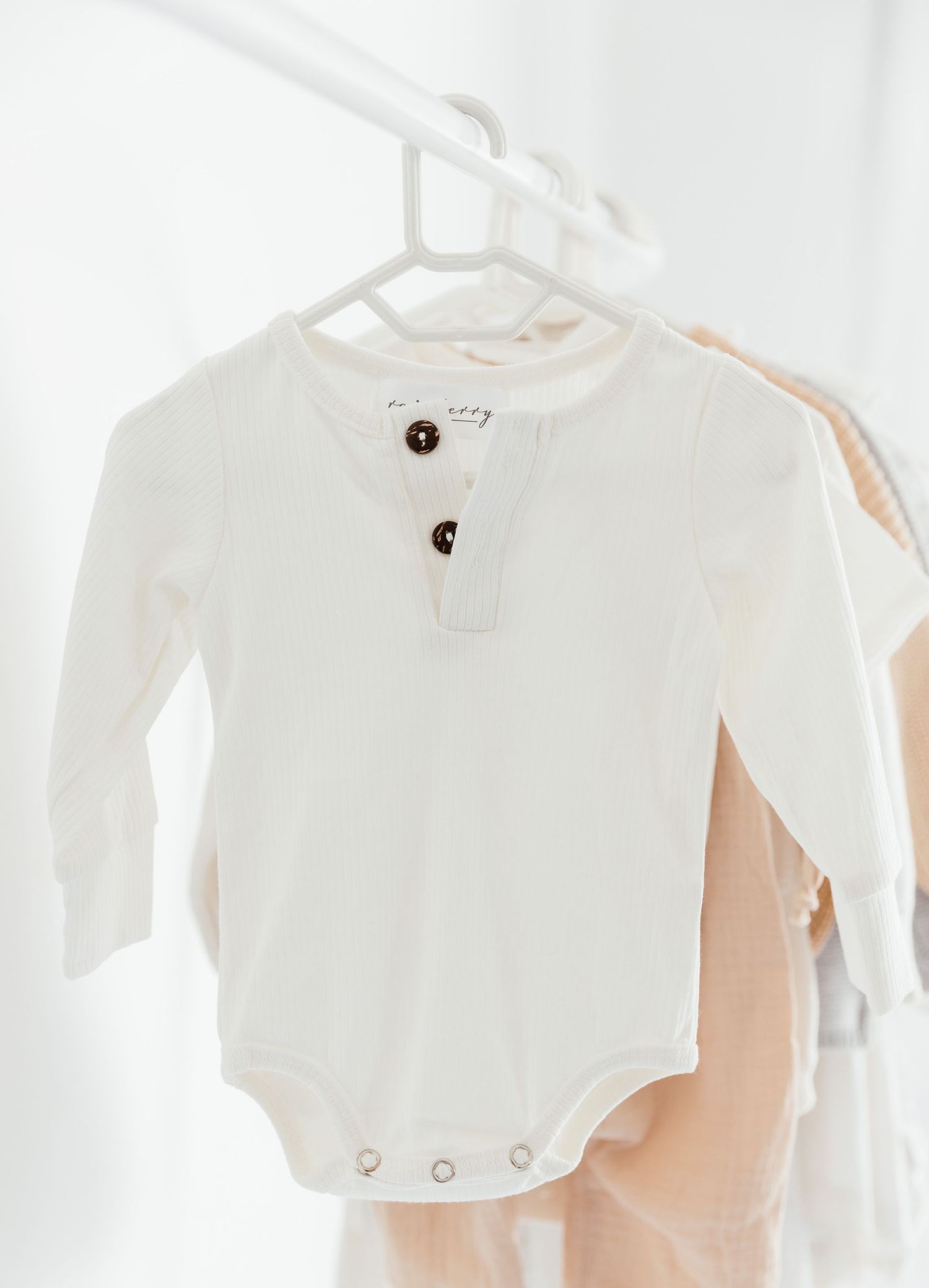 White cotton baby onesie with buttons hanging on a white hanger.