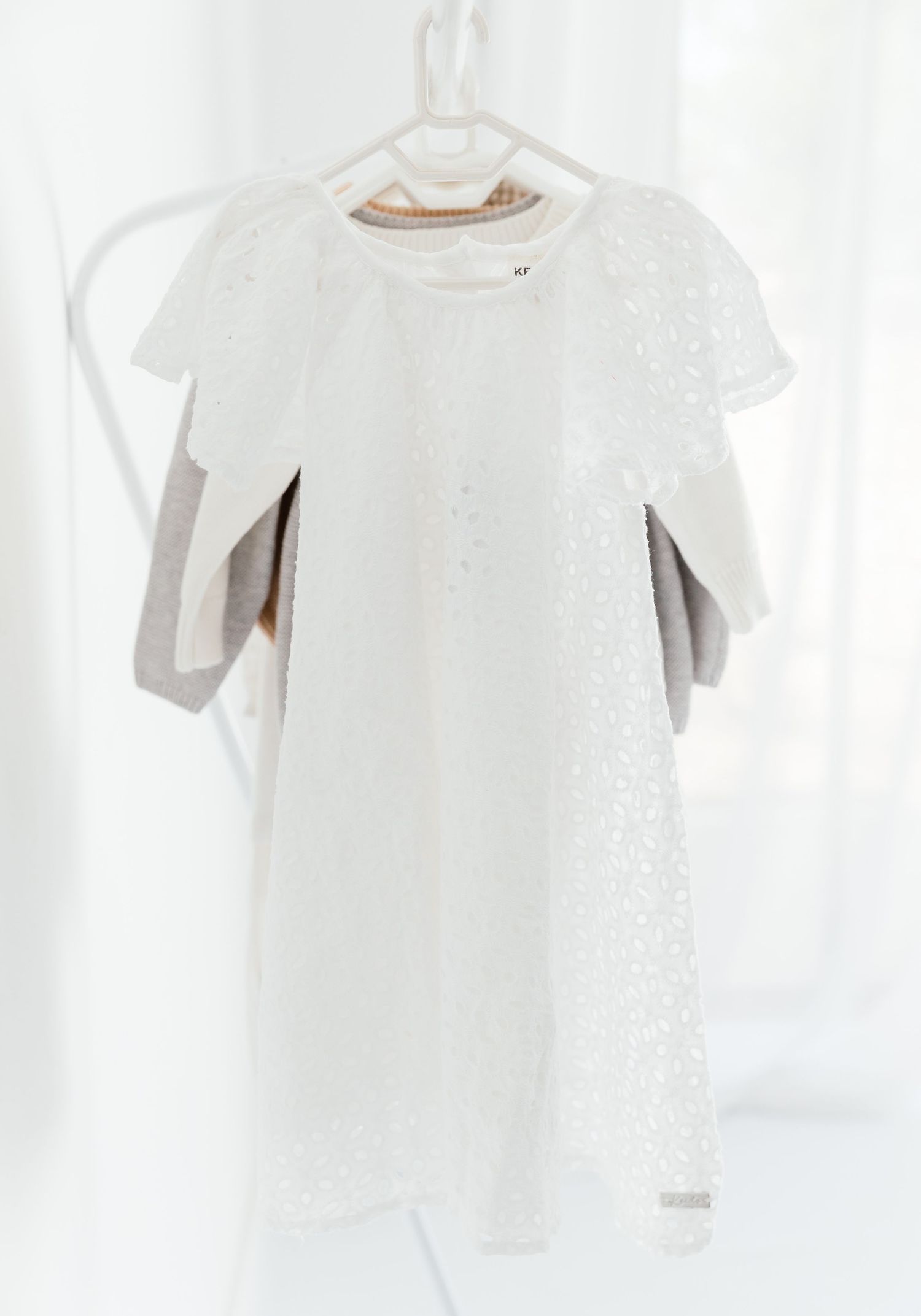 White lacey dress hanging on white hanger against light background.
