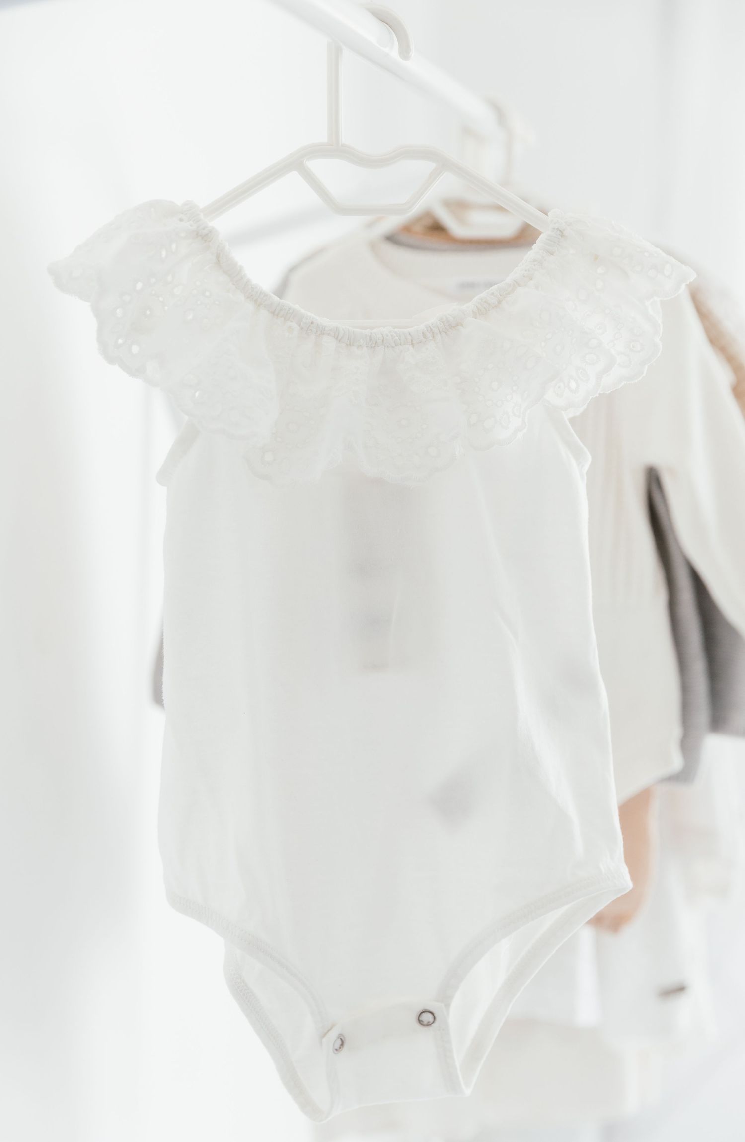 White lace trimmed baby onesie displayed on hanger.