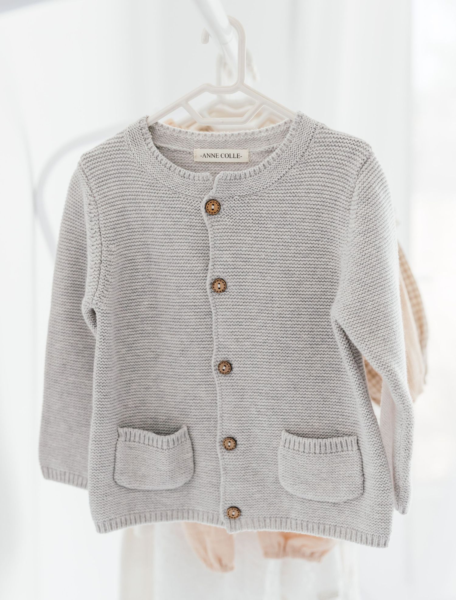 Gray knit baby cardigan with pockets and wooden buttons hanging on white hanger.