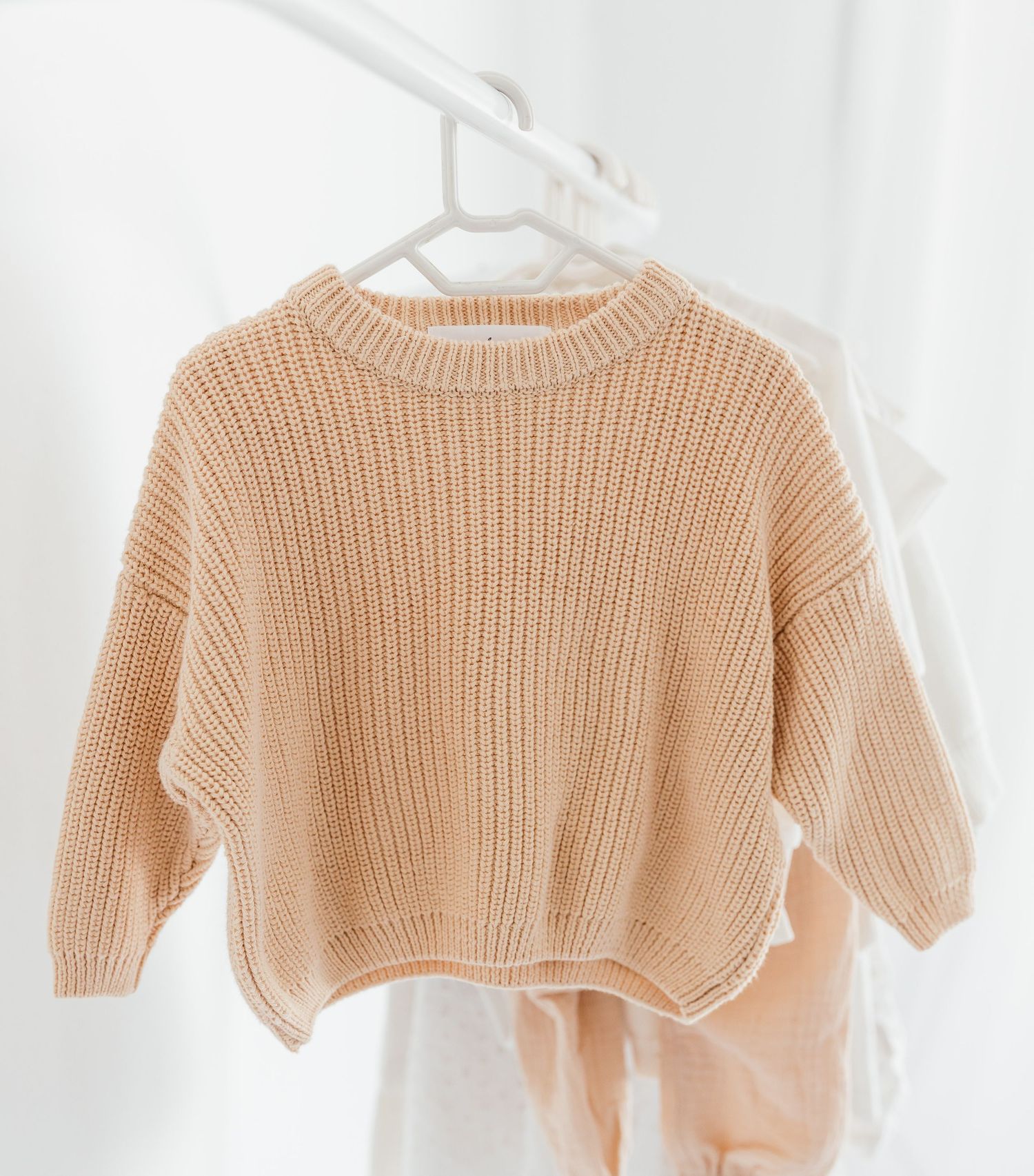 Beige knit sweater hanging on white hanger against light background.