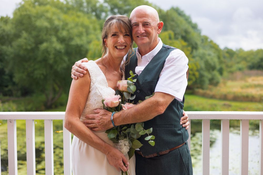 Bride and groom share a hug on the balcony overlooking the pond at Arrow Mill.
