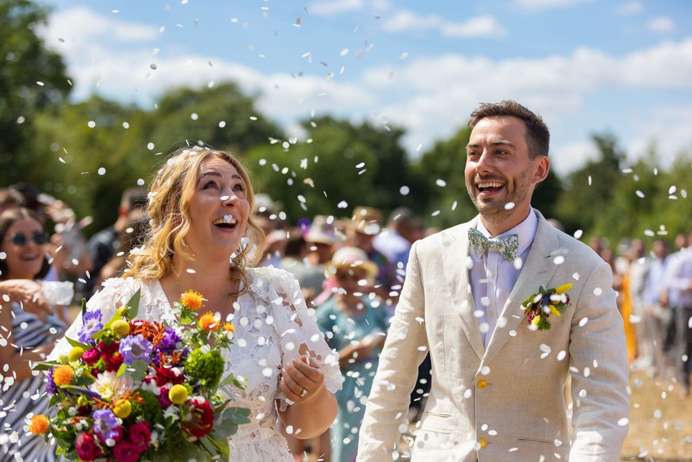 Bride and groom look on in amazement as confetti falls around them.