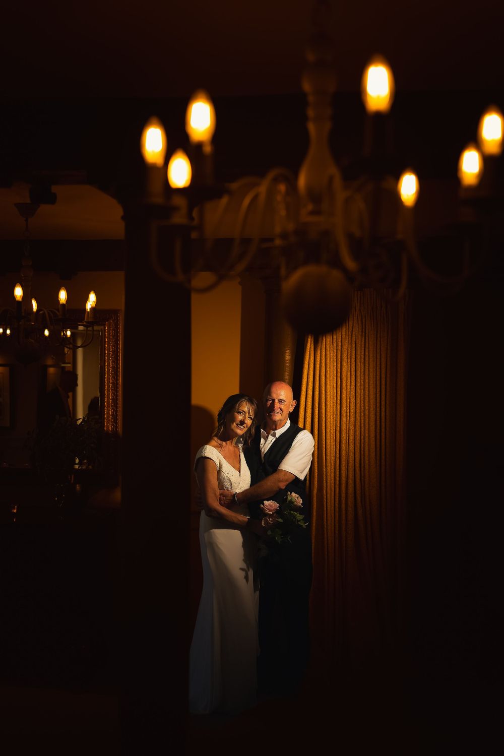 A low-light bride and groom portrait with the couple lit up below a chandelier.