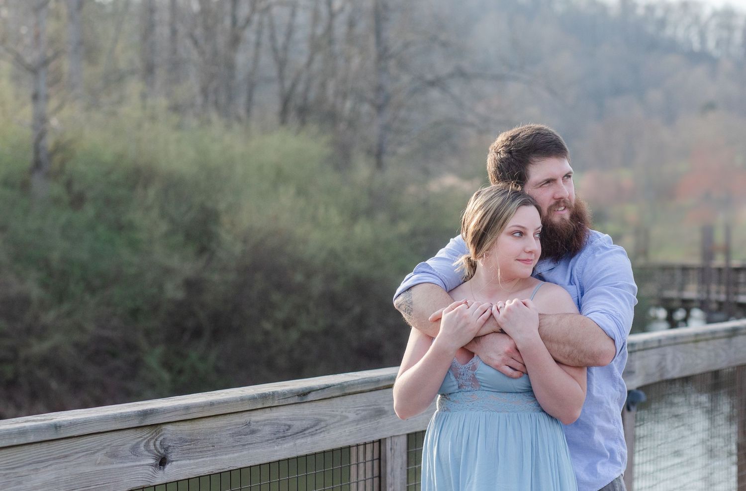 Two people share intimate moments along a wooden bridge with water views.