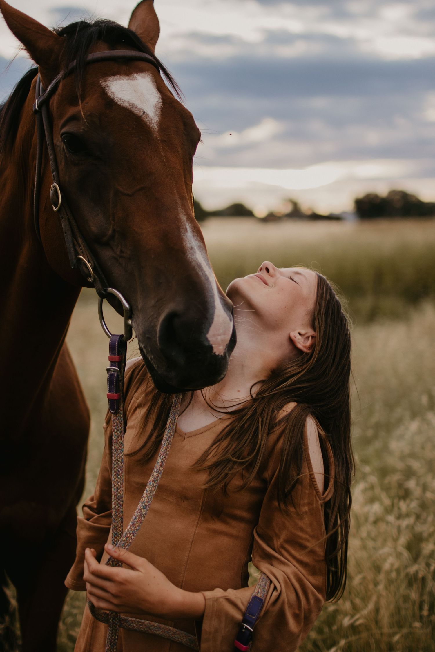 a girl stand next her horse who is nuzzling her neck, in a rural paddock
