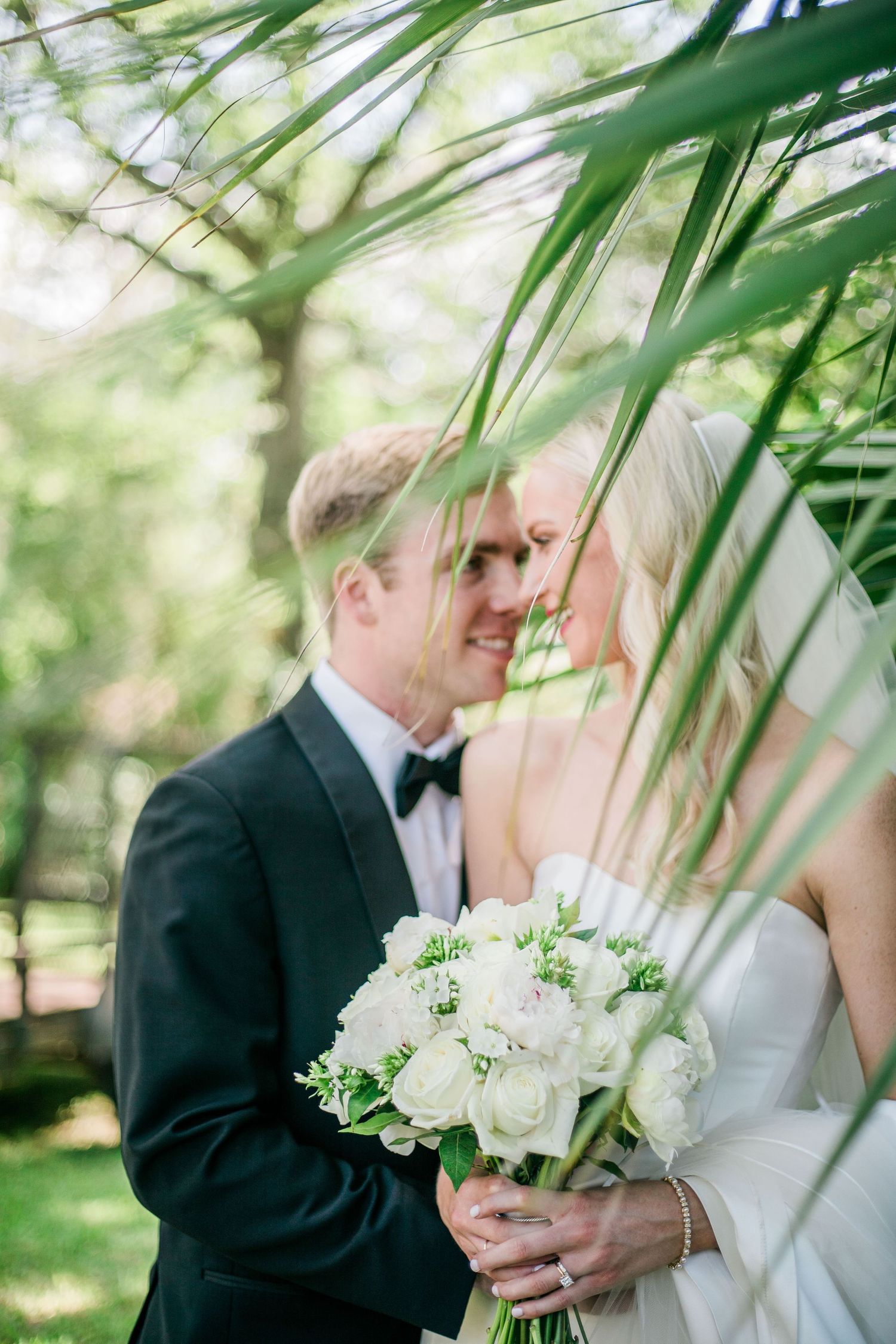 A romantic wedding moment framed by soft green palm fronds.