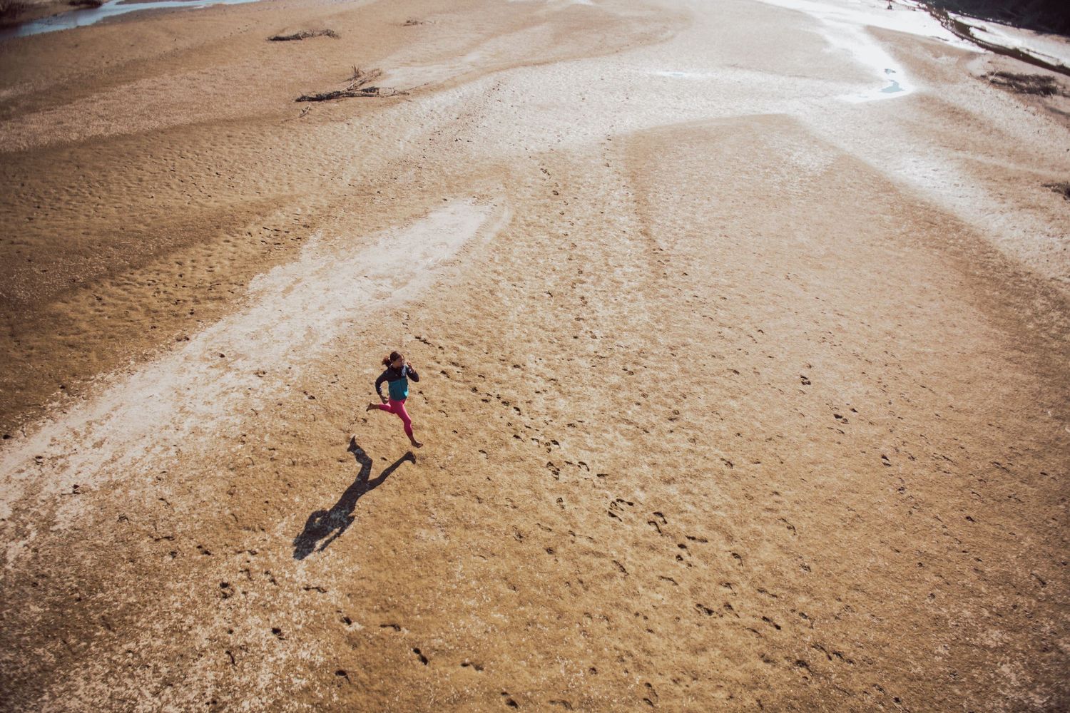 Aerial view of a lone runner casting long shadow on desert sand terrain during golden hour light.