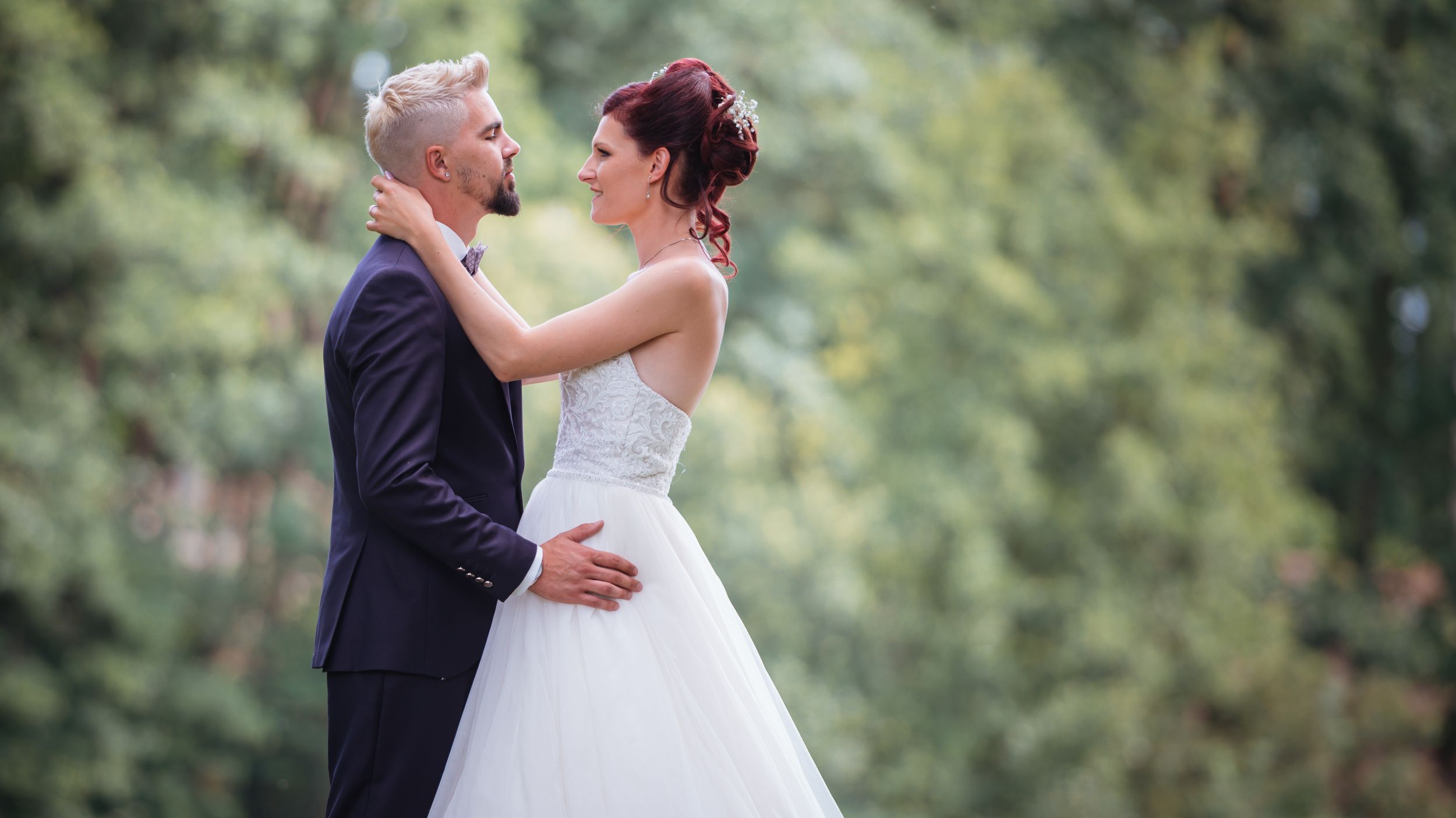 Elegant bride and groom share a romantic moment in a lush green outdoor setting on their wedding day.