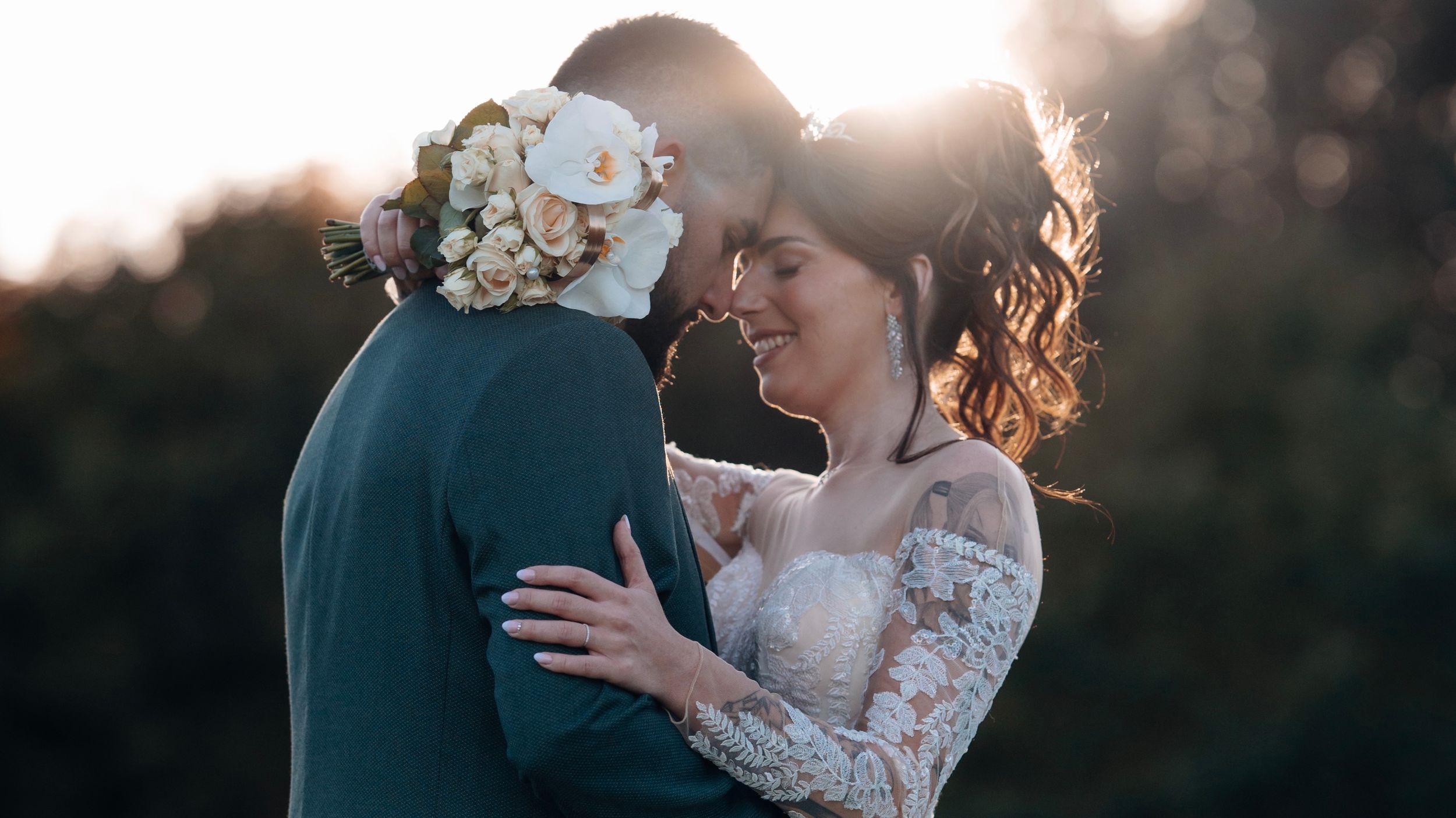Bride and groom sharing a romantic moment at golden hour with a floral bouquet.