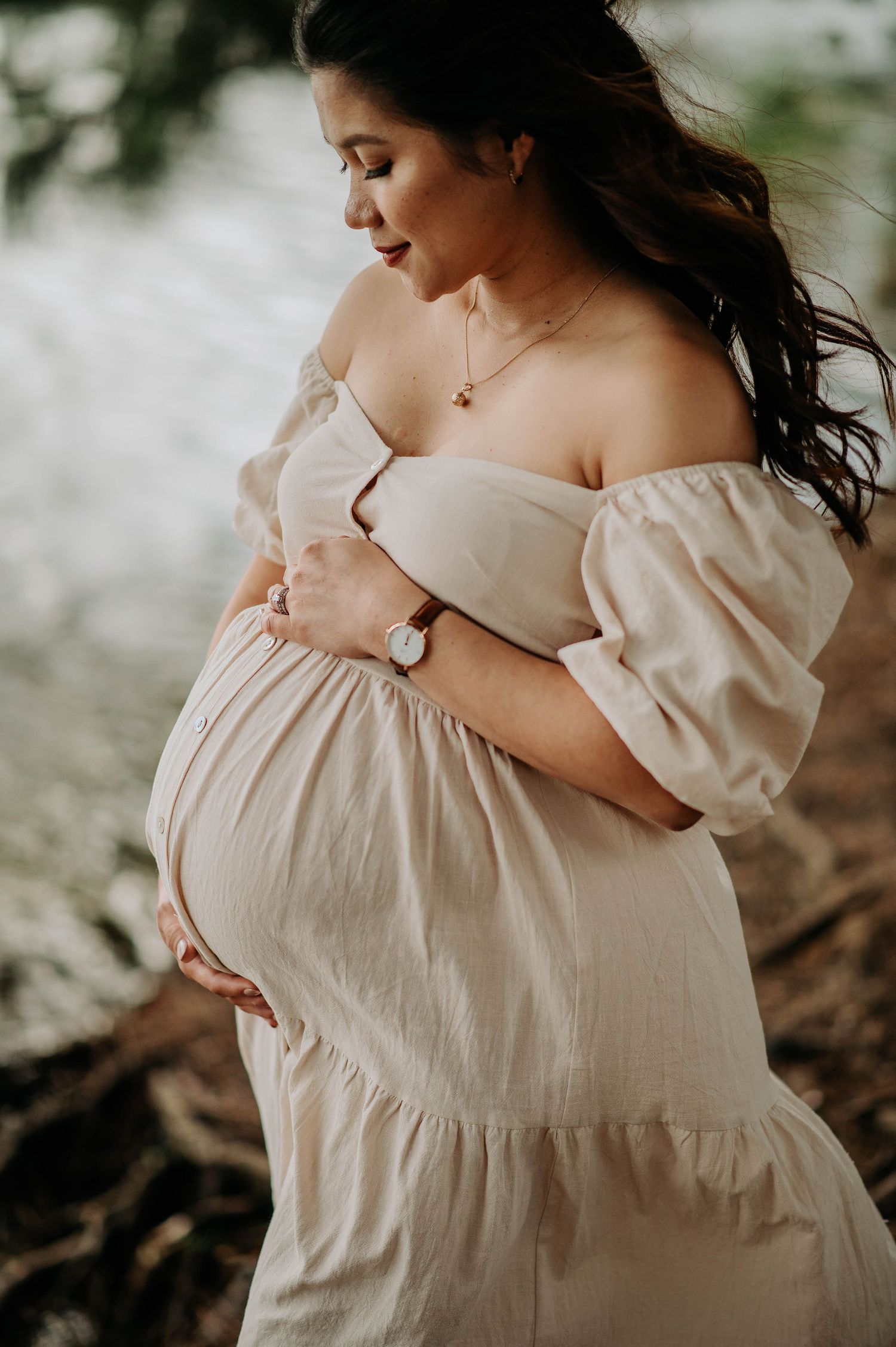Side profile of expectant mother in flowing cream dress touching her baby bump.