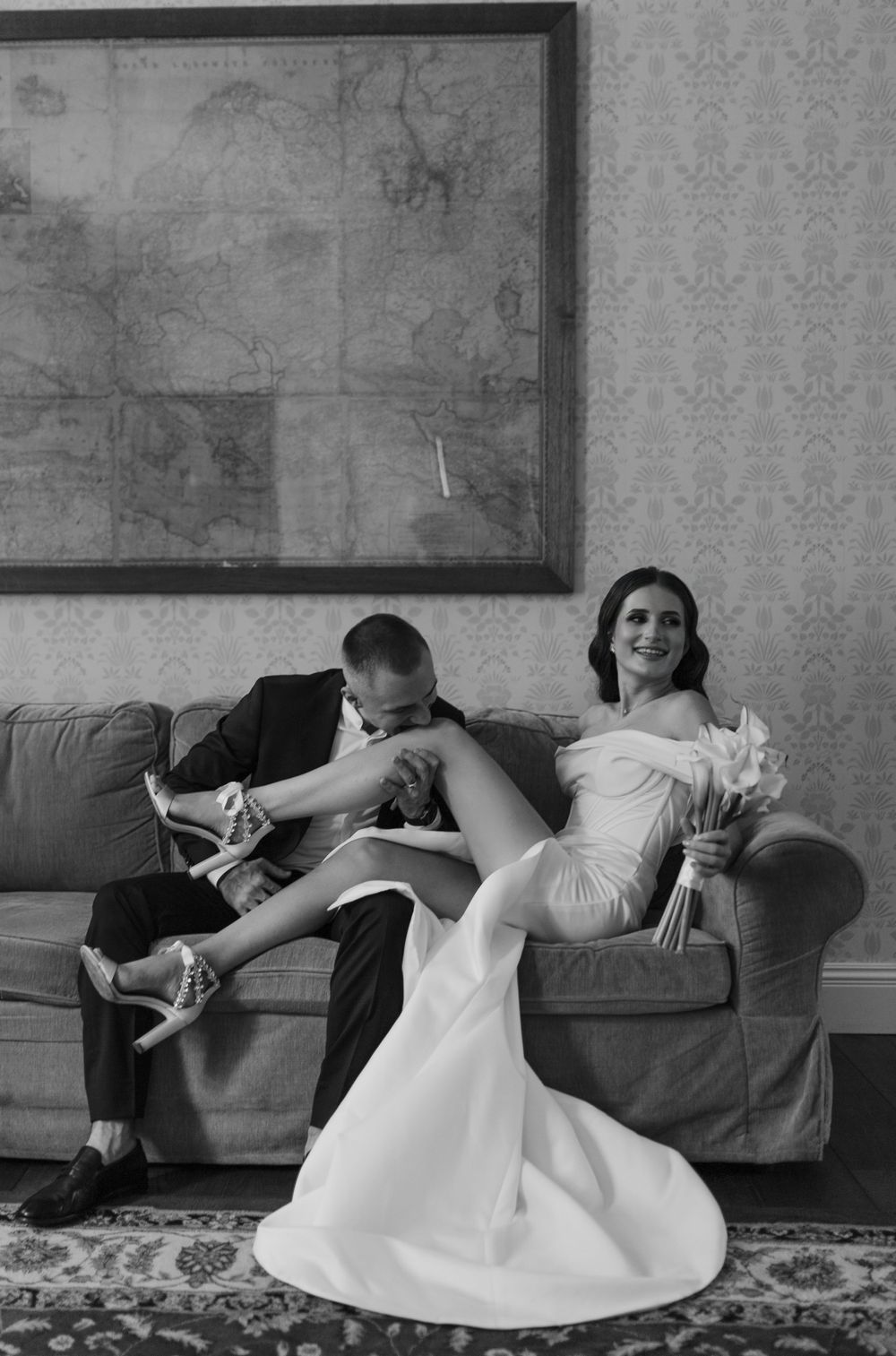 Black and white wedding photo of couple relaxing casually on gray sofa.