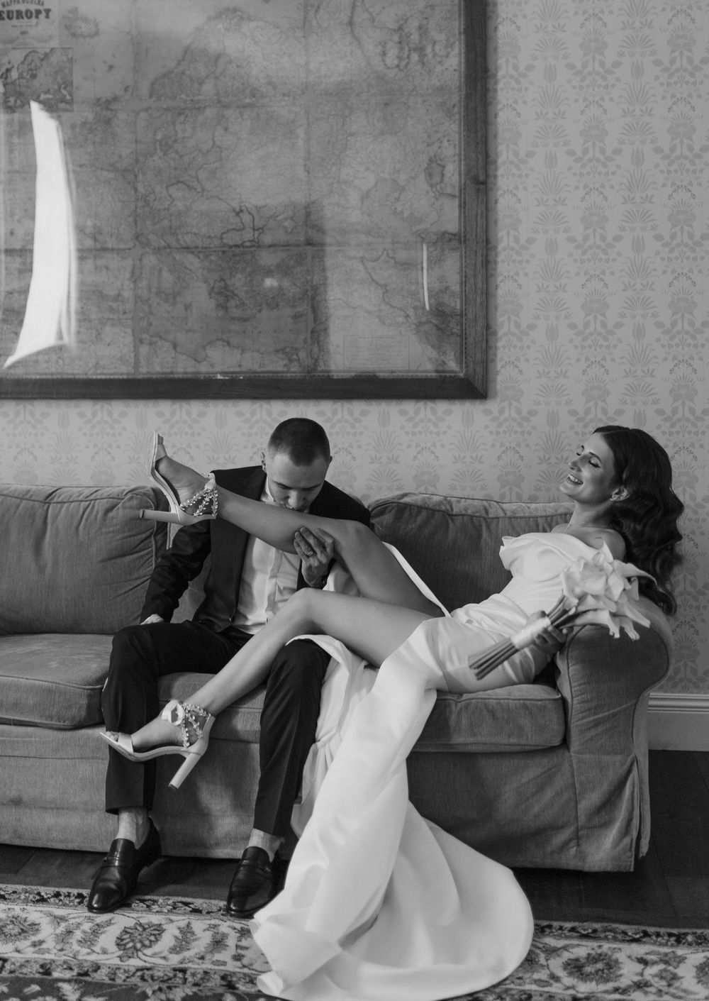 Artistic black and white photo of newlyweds lounging playfully on couch.