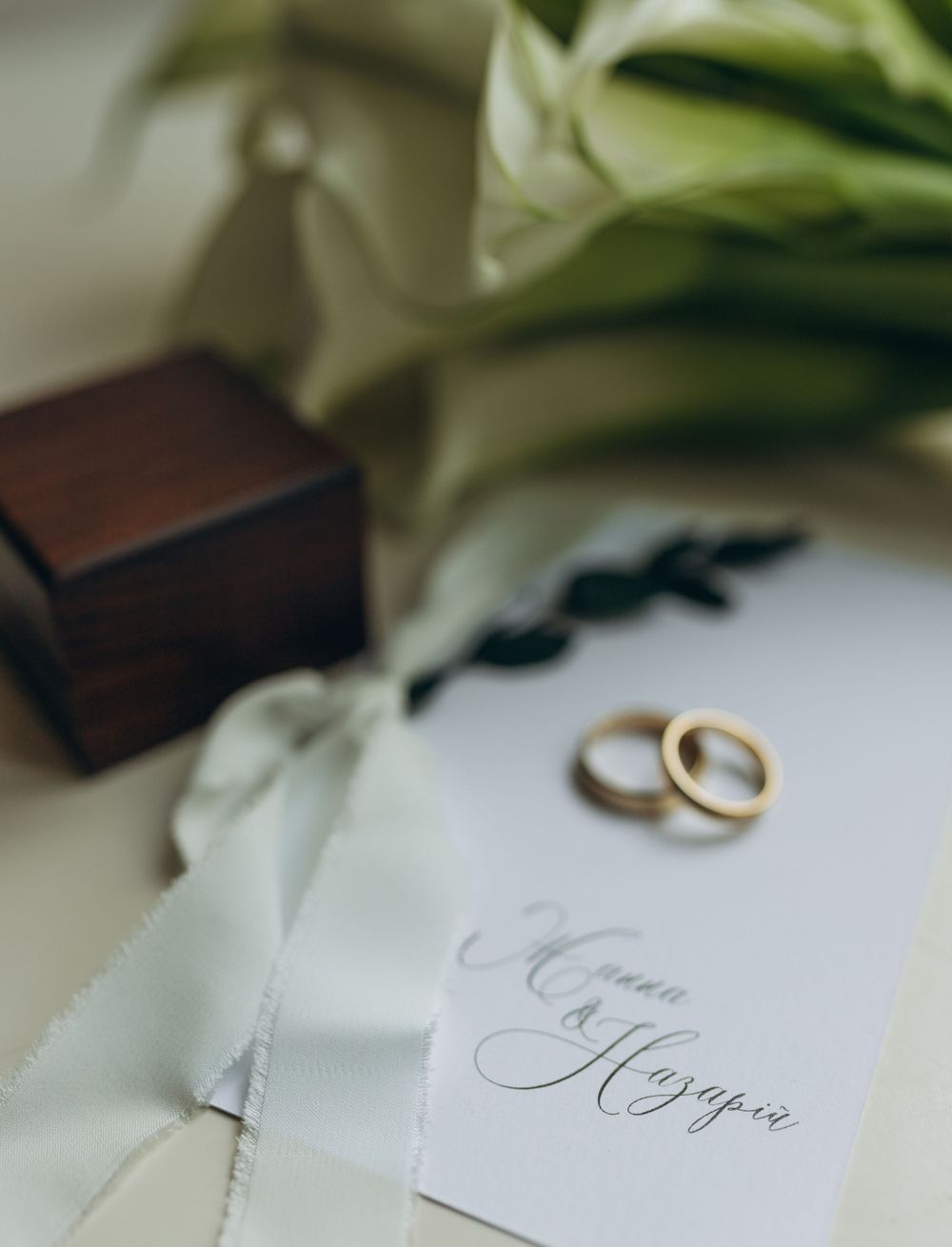 Wedding detail shot of gold rings, wooden box and calligraphy card with floral accents.