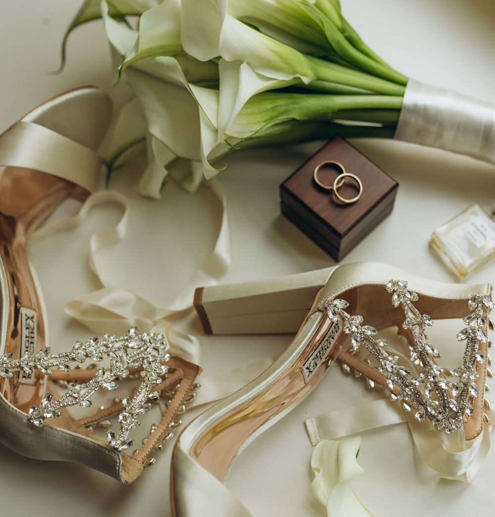 Wedding accessories including embellished heels, rings, perfume and white calla lily bouquet.