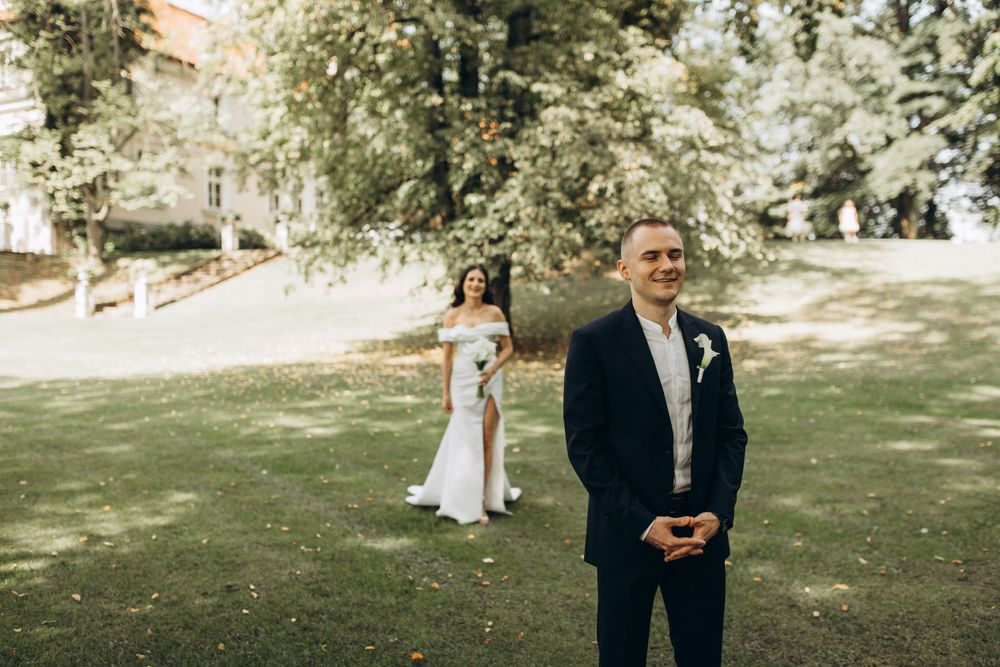 Wedding day scene outdoors with couple standing apart in sunlit garden.