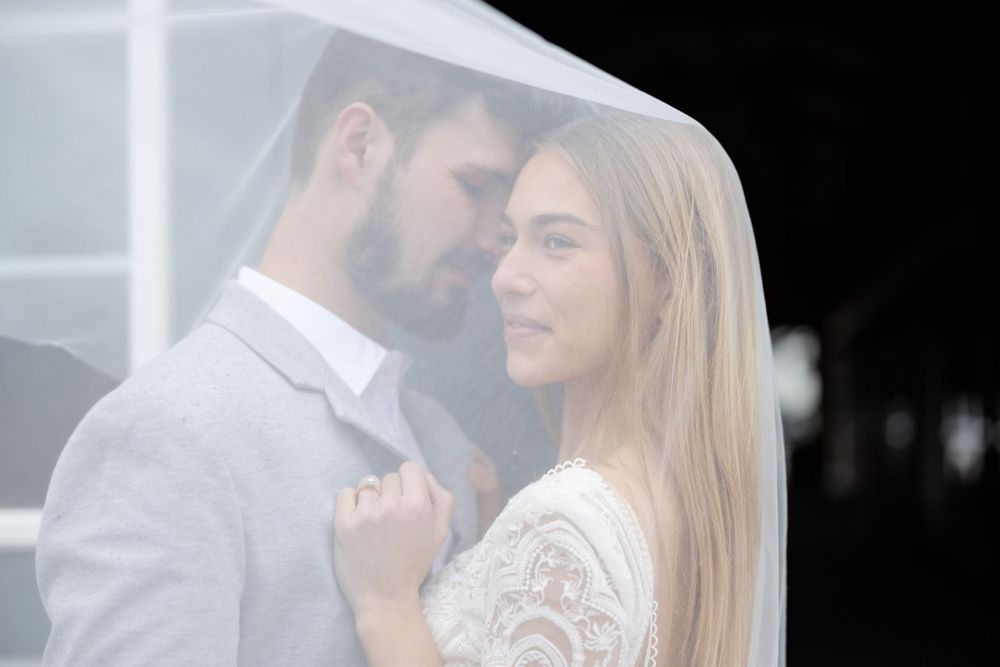 A romantic moment between a couple under a white veil with soft lighting.