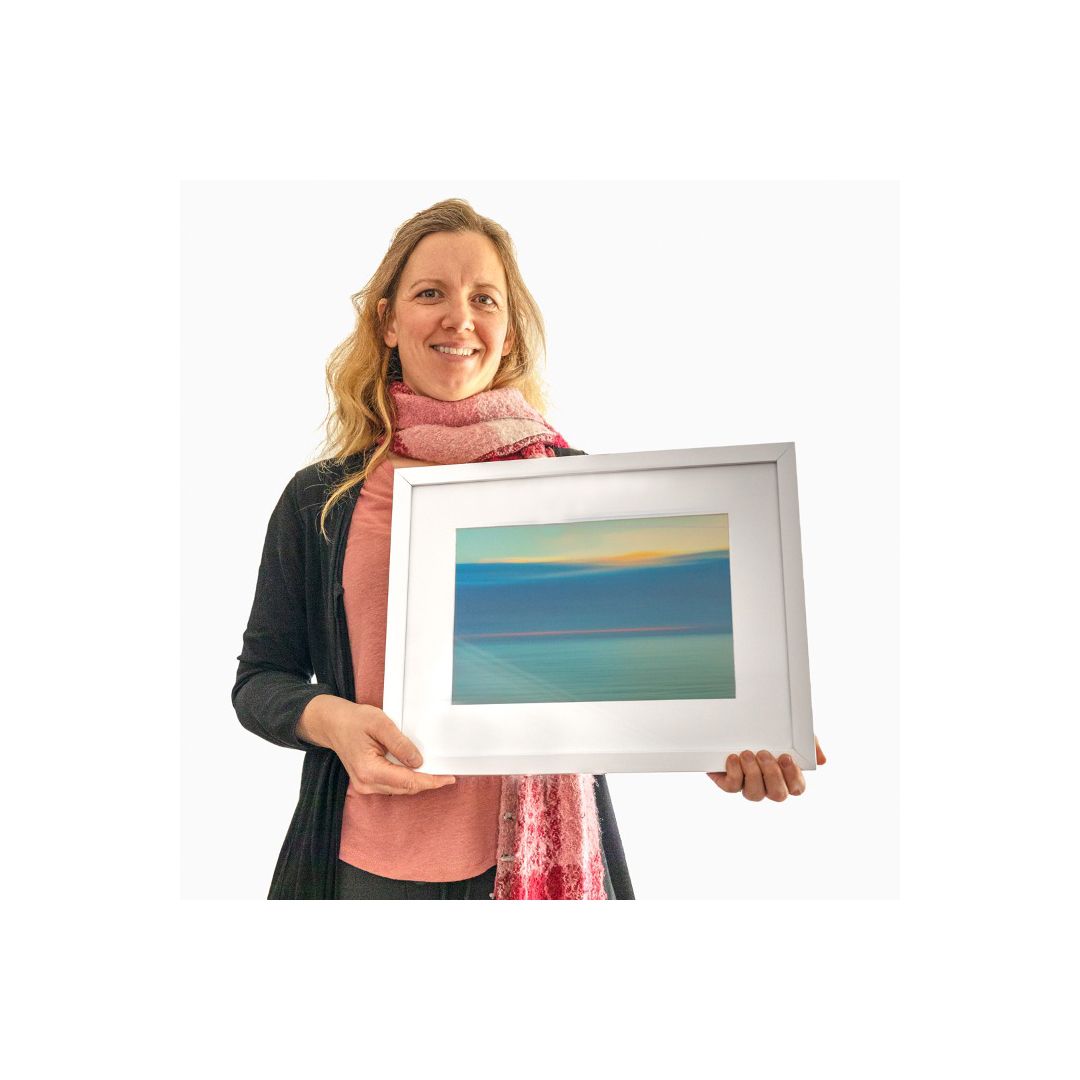 Person holding framed abstract landscape artwork featuring blue and turquoise gradient colors.