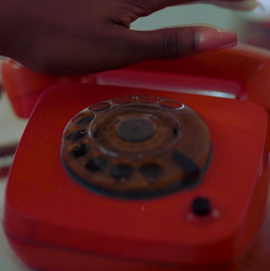 A close-up shot of someone's hand near a vintage red rotary telephone dial.