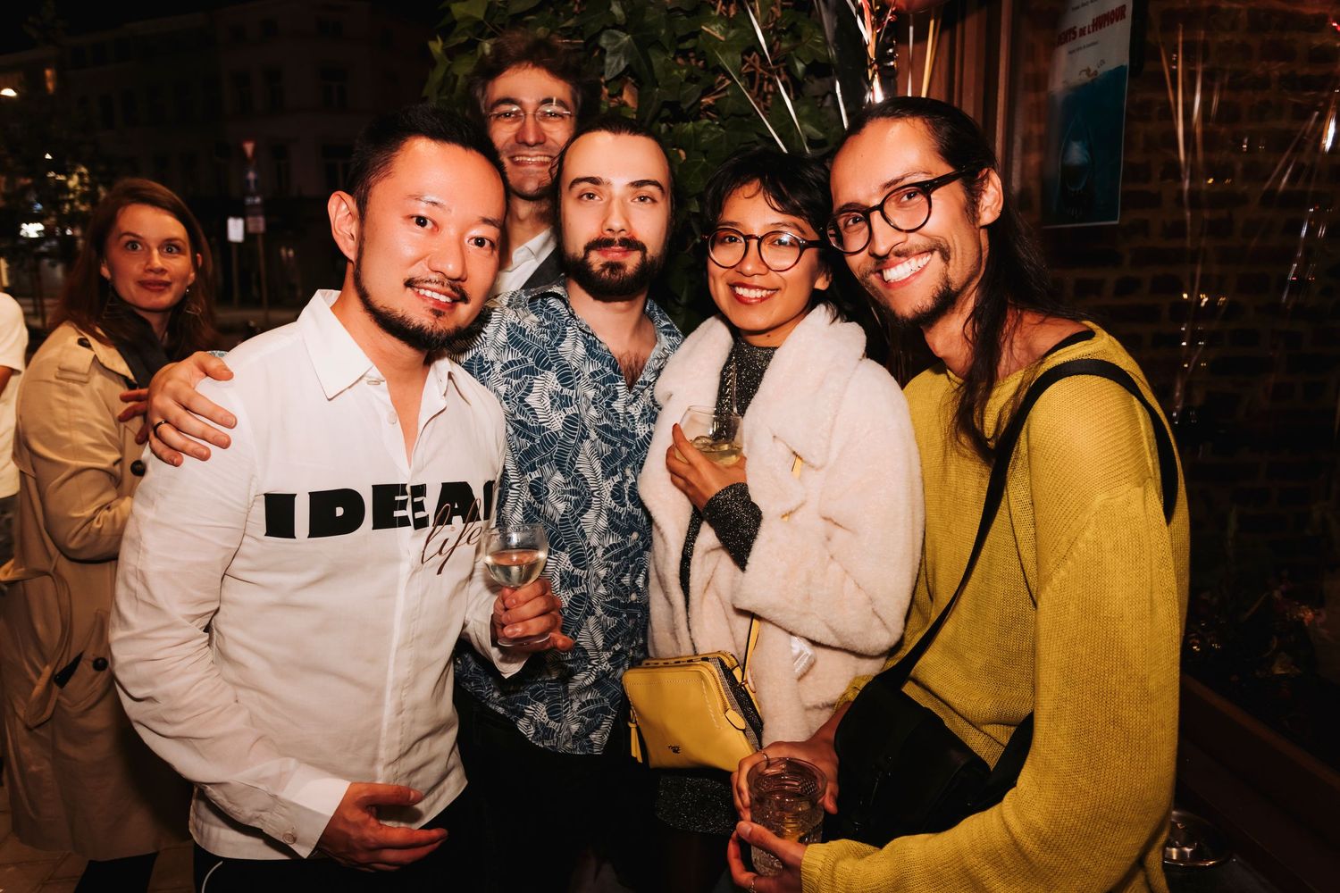 A group of friends smile and pose together at a nighttime social gathering.