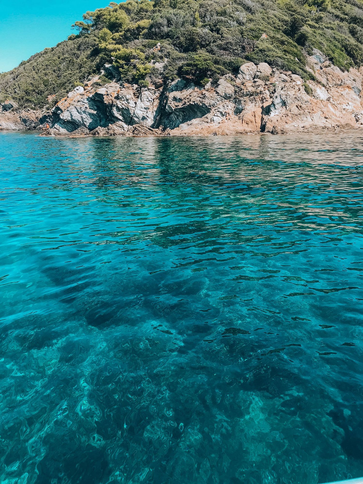 Crystal clear turquoise waters meeting rocky coastline under bright blue skies.