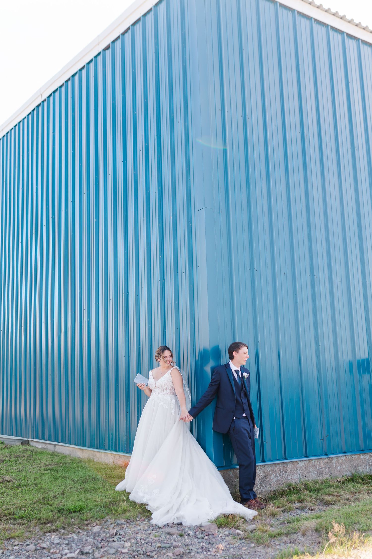 Wedding couple poses against bright blue industrial building for artistic portrait.