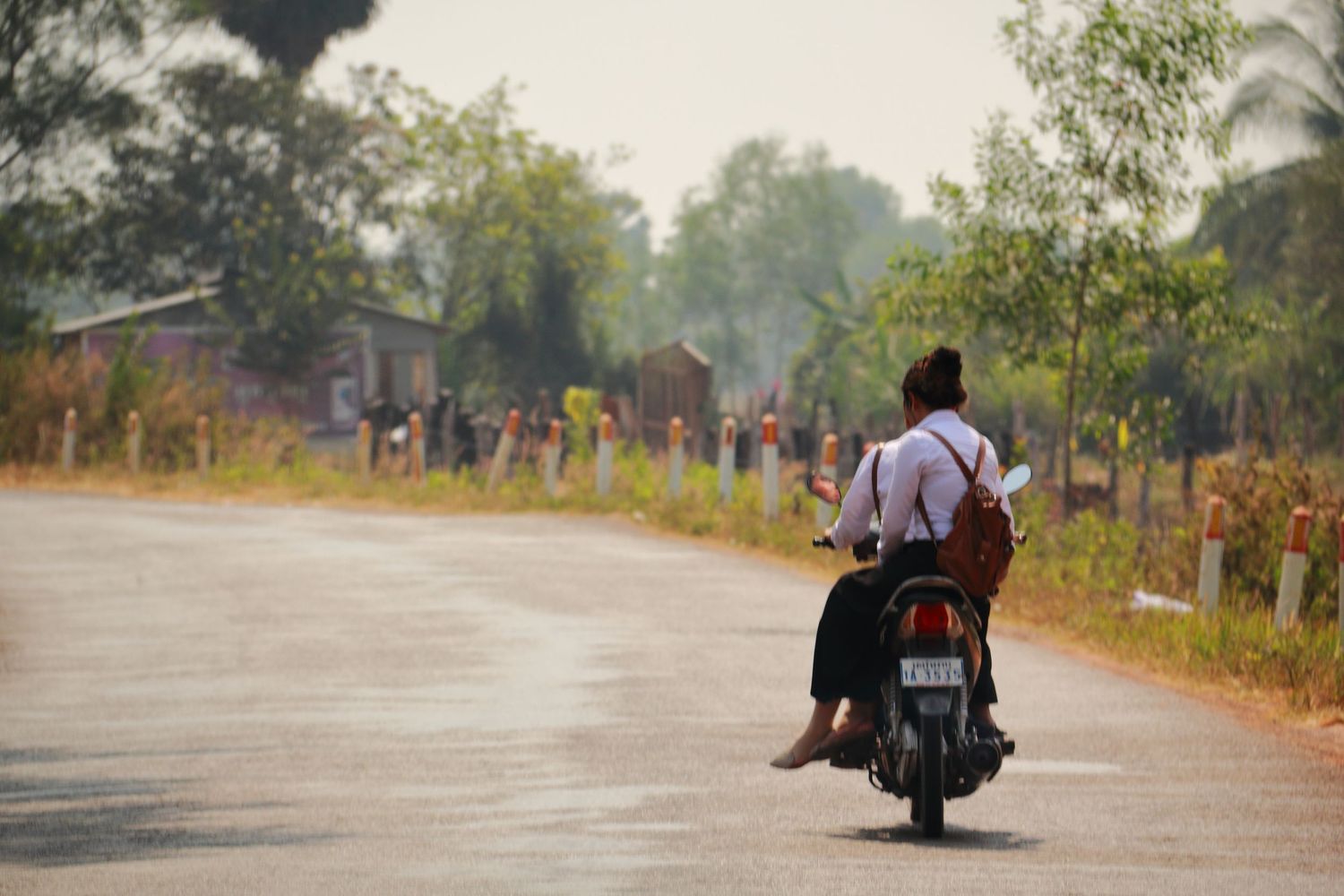 Motorcyclist riding on a rural road with figures walking in the background.