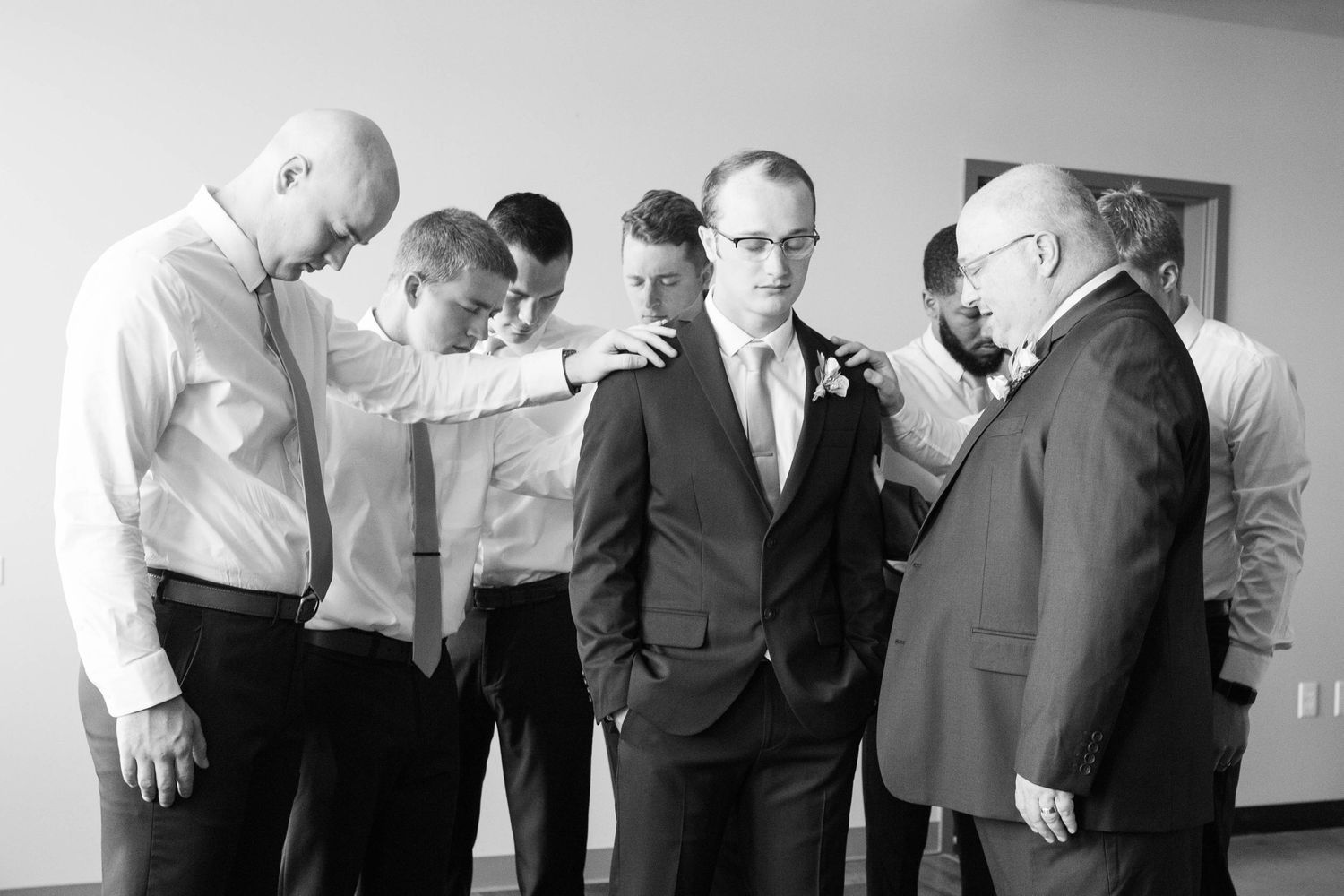 Grooms father and groomsmen praying over groom