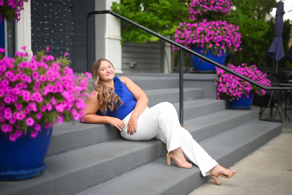 Woman in white dress poses near bright pink flowers and concrete steps.
