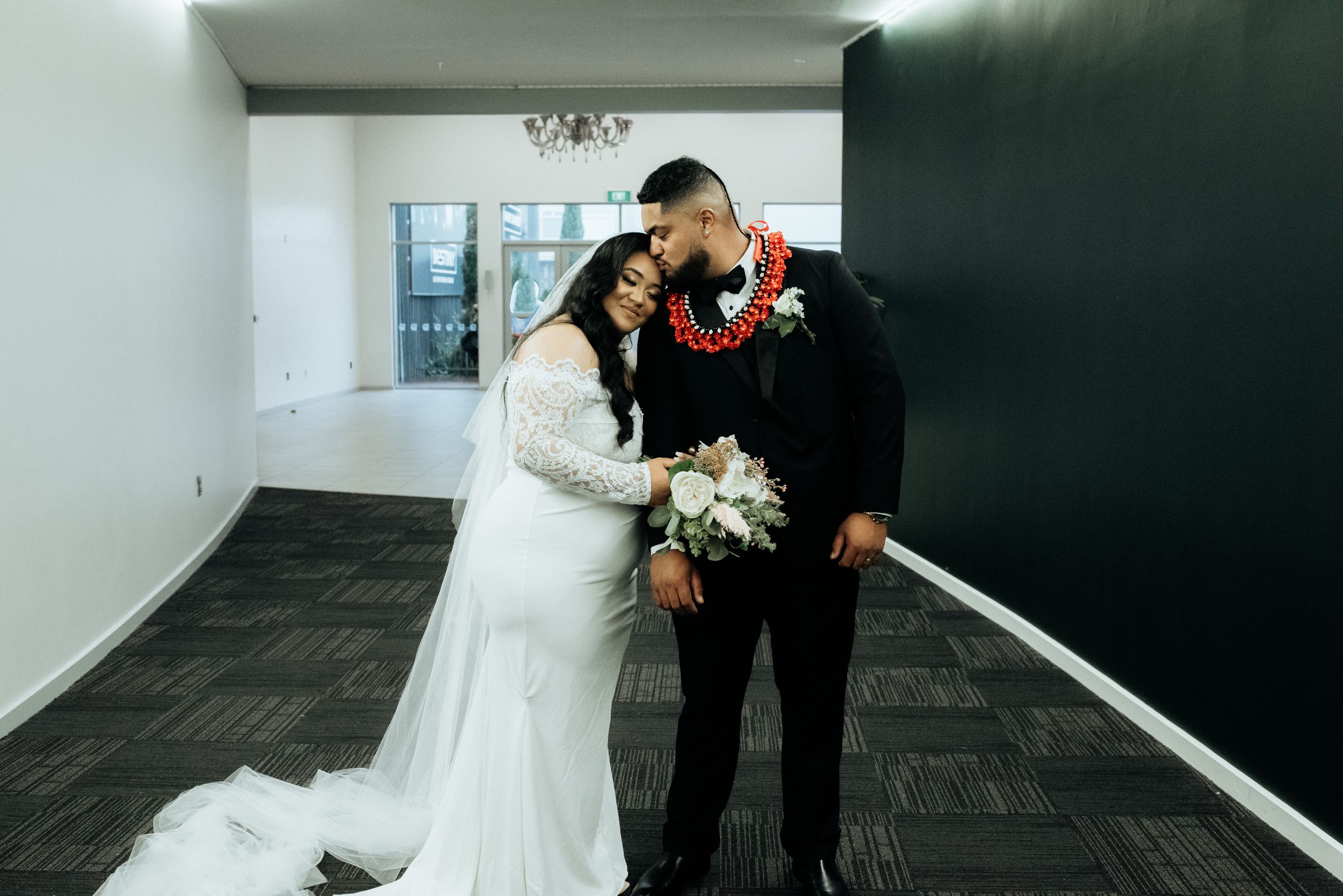 Bride and groom share a tender kiss while holding a bouquet in a modern indoor venue.