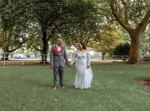 Bride and groom holding hands walking through lush green park on their wedding day.